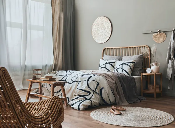 Yatak odasının içinde ahşap yatak odası, mobilya, vazoda kurutulmuş çiçekler, rattan dekorasyon ve zarif aksesuarlarla süslenmiş şık bir kompozisyon. Güzel çarşaflar, battaniye ve yastıklar. Konforlu ev dekorasyonu. 