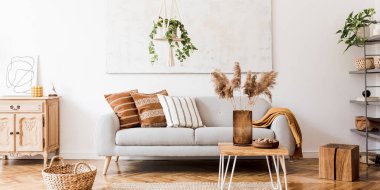 Gri kanepe, kahve masası, bitkiler, halı ve güzel aksesuarlarla birlikte yaratıcı ve rahat bir oturma odası kompozisyonu. Beyaz duvarlar ve parke zemin.