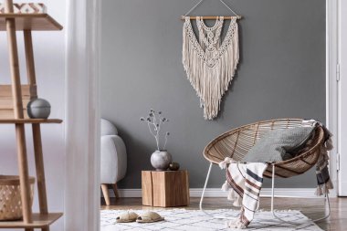 Kahve masası, rattan koltuğu, bitkiler, halı ve güzel boho aksesuarları olan yaratıcı ve rahat bir oturma odası kompozisyonu. Okaliptüs duvarları ve parke zemin. 