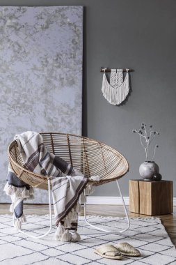 Kahve masası, rattan koltuğu, bitkiler, halı ve güzel boho aksesuarları olan yaratıcı ve rahat bir oturma odası kompozisyonu. Okaliptüs duvarları ve parke zemin. 