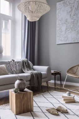 Kahve masası, rattan koltuğu, bitkiler, halı ve güzel boho aksesuarları olan yaratıcı ve rahat bir oturma odası kompozisyonu. Okaliptüs duvarları ve parke zemin. 