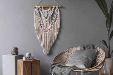 Kahve masası, rattan koltuğu, bitkiler, halı ve güzel boho aksesuarları olan yaratıcı ve rahat bir oturma odası kompozisyonu. Okaliptüs duvarları ve parke zemin. 