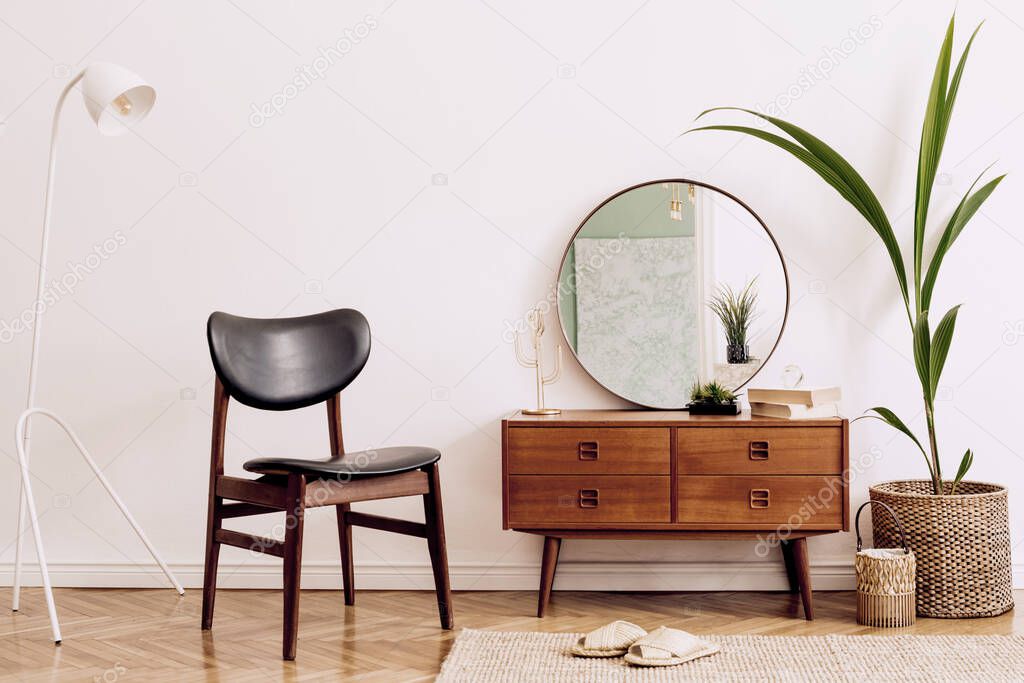 Minimalistic and stylish composition of living room with wooden commode, mirror, chair , lamp, tropicla plant in rattan basket and elegant personal accessories. Interior design, Home decor. template.