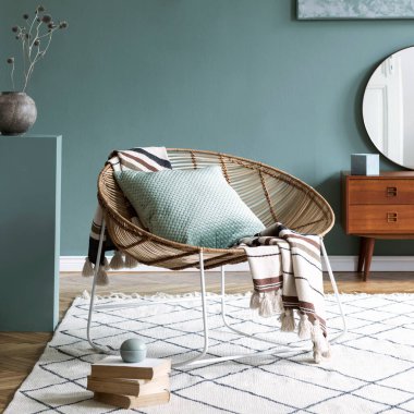 Kahve masası, rattan koltuğu, bitkiler, halı ve güzel boho aksesuarları olan yaratıcı ve rahat bir oturma odası kompozisyonu. Okaliptüs duvarları ve parke zemin. 