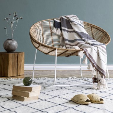 Kahve masası, rattan koltuğu, bitkiler, halı ve güzel boho aksesuarları olan yaratıcı ve rahat bir oturma odası kompozisyonu. Okaliptüs duvarları ve parke zemin. 