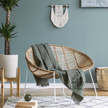 Kahve masası, rattan koltuğu, bitkiler, halı ve güzel boho aksesuarları olan yaratıcı ve rahat bir oturma odası kompozisyonu. Okaliptüs duvarları ve parke zemin. 