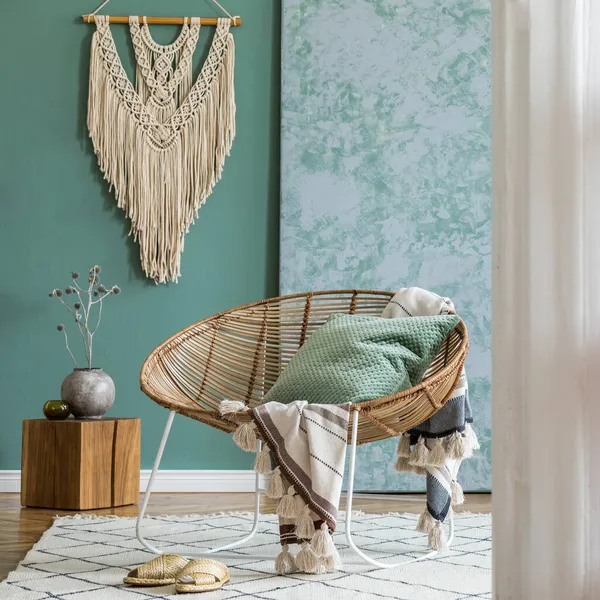 Kahve masası, rattan koltuğu, bitkiler, halı ve güzel boho aksesuarları olan yaratıcı ve rahat bir oturma odası kompozisyonu. Okaliptüs duvarları ve parke zemin. 