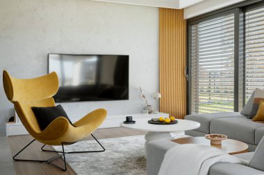 Köşedeki bej kanepe, sarı koltuk, sehpa ve minimalist aksesuarlarla oturma odasının şık kompozisyonu. Panoramik pencere. Şablon