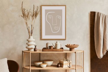 Creative interior composition with design wooden console, mock up poster frame, armchair and stylish personal accessories such as teapot, vase and books. Copy space. Template
