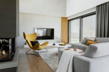 Creative living room interior composition with corner sofa,  yellow armchair, fireplace and personal accessories. Panoramic window. Template.