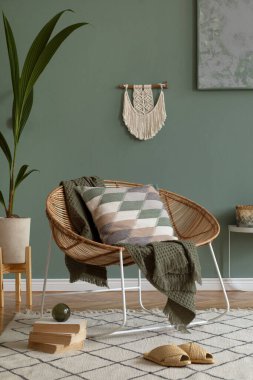Kahve masası, rattan koltuğu, bitkiler, halı ve güzel boho aksesuarları olan yaratıcı ve rahat bir oturma odası kompozisyonu. Yeşil duvarlar ve parke zemin. Uzayı kopyala Şablon