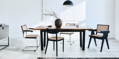 Ahşap masa, dizayn sandalyeleri, vazoda kurumuş çiçekler, siyah kolye lambası, duvarda resim resimleri ve zarif kişisel aksesuarlarla yemek odasının minimalist kompozisyonu. Şablon.