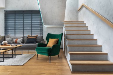 Köşedeki gri kanepe, yeşil kadife koltuk, sehpa, ahşap zemin, tasarım mobilyaları ve minimalist kişisel aksesuarlarla oturma odasının şık kompozisyonu. Modern ev dekorasyonu. Şablon.