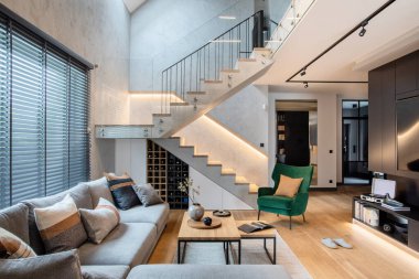 Köşedeki gri kanepe, yeşil kadife koltuk, sehpa, ahşap zemin, tasarım mobilyaları ve minimalist kişisel aksesuarlarla oturma odasının şık kompozisyonu. Modern ev dekorasyonu. Şablon.