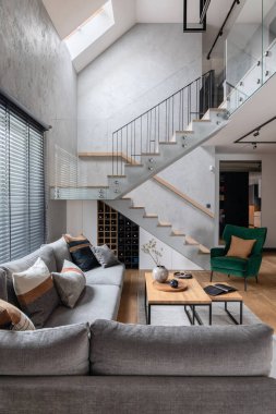 Köşedeki gri kanepe, yeşil kadife koltuk, sehpa, ahşap zemin, tasarım mobilyaları ve minimalist kişisel aksesuarlarla oturma odasının şık kompozisyonu. Modern ev dekorasyonu. Şablon.