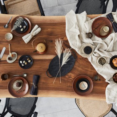 Ahşap ceviz masası, retro sandalyeler, sofra takımı, tabaklar, masa örtüsü, çaydanlık, yemek, dekorasyon ve zarif aksesuarları olan şık bir iç dizayn. Beton zemin. Şablon. Üst görünüm.