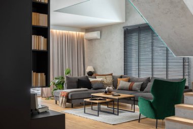 Köşedeki gri kanepe, yeşil kadife koltuk, sehpa, ahşap döşeme, tasarım mobilya ve kişisel aksesuarlarla oturma odasının şık kompozisyonu. Modern ev dekorasyonu. Şablon.