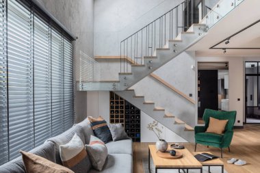 Oturma odasının içindeki merdivenlerin şık kompozisyonu. Gri kanepe, yeşil kadife koltuk, sehpa ve minimalist kişisel aksesuarlar. Modern ev dekorasyonu. Şablon.