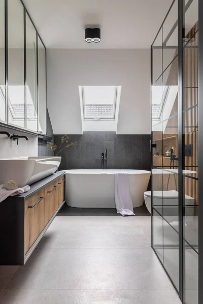 Stylish interior of bathroom with bathtub, shower, towels and other personal bathroom accessories. Modern and design interior. Marble walls. Roof window. Template.