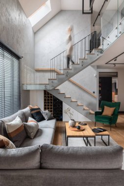 Oturma odasının içinde merdivenleri olan şık bir kompozisyon. Gri kanepe, yeşil kadife koltuk, sehpa ve minimalist kişisel aksesuarlar. Modern ev dekorasyonu. Şablon.