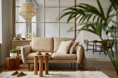 Bej renkli modern kanepe, sehpa ve yaratıcı aksesuarları olan zarif bir oturma odası iç tasarımı. Şablon. Uzayı kopyala Arka tarafta yemek odası var..