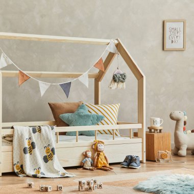 Ahşap yatak, raf, peluş ve ahşap oyuncaklar ve tekstil asma süslemeleriyle İskandinav çocuk odasının iç kısmının şık kompozisyonu. Tarafsız yaratıcı duvar, yerde halı. Şablon.