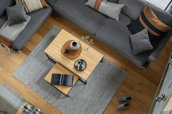 Stylish top view composition of living room interior with corner grey sofa, coffee table, carpet and minimalist personal accessories. Modern home decor.  Parquet floor. Template.