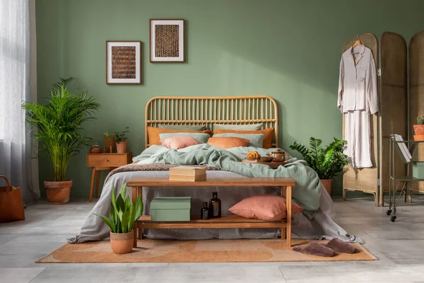 Stylish bedroom interior design with mock up poster frame, bamboo bed, night table, plants, folding screen and creative home accessories. Eucalyptus wall. Template. Copy space.