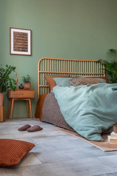 Stylish bedroom interior design with mock up poster frame, bamboo bed, night table, plants and creative home accessories. Eucalyptus wall. Home staging. Template. Copy space.