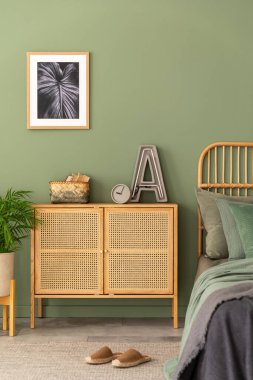 Modern yatak odasının iç kısmının şık bir kompozisyonu. Poster çerçevesi, rattan klozet, güzel çarşaflar ve yaratıcı kişisel aksesuarlar. Sgae yeşil duvarı. Şablon. Boşluğu kopyala.