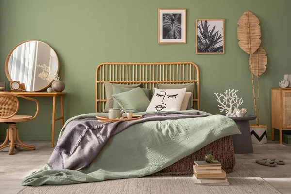 Stylish bedroom interior design with mock up poster frames, bed, side table, rattan commode, vanity table and creative home accessories. Sage green wall. Template. Copy space
