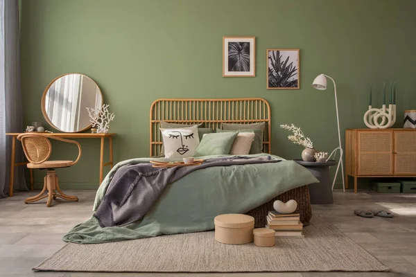 Stylish bedroom interior design with mock up poster frames, bed, side table, rattan commode, vanity table and creative home accessories. Sage green wall. Template. Copy space