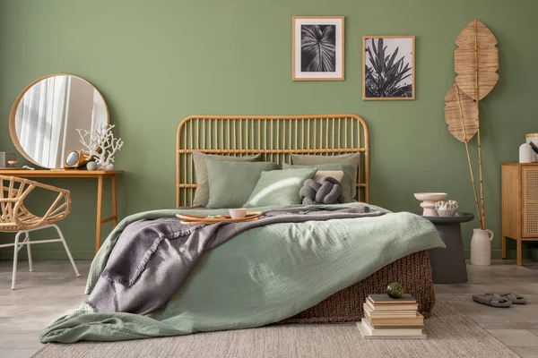 Stylish bedroom interior design with mock up poster frames, bed, side table, rattan commode, vanity table and creative home accessories. Sage green wall. Template. Copy space