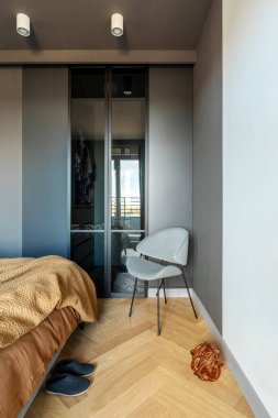 Modern yatak odasının iç kısmının şık bir kompozisyonu. Gardırop, gri sandalye ve zarif kişisel aksesuarlar. Gri duvar. Kahverengi çarşaflar. Minimalist erkeksi kavram. Şablon.