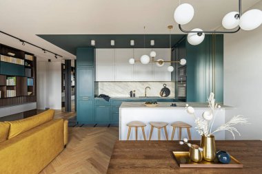 Lüks modern ve klasik turkuaz iç mimari. Ahşap çengelli mermer mutfak adası. Kahverengi ahşap masa, metal tepsi ve beyaz süslemeli metalik altın vazo.. 