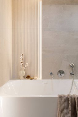 Lamella duvarlı, modern, parlak banyo. Gümüş musluğu ve kahverengi havlusu olan büyük beyaz bir banyo.. 