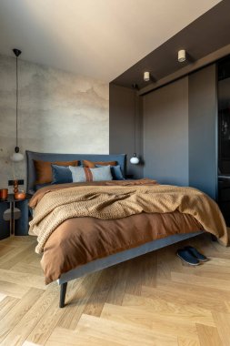Modern yatak odasının iç kısmının şık bir kompozisyonu. Yatak, yaratıcı lamba ve zarif kişisel aksesuarlar. Beton duvar. Kahverengi çarşaflar. Minimalist erkeksi kavram. Şablon.