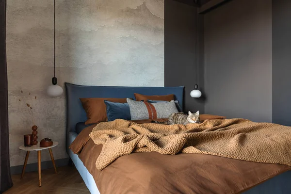 Stylish composition of modern bedroom interior. Bed, creative lamp and elegant personal accessories. Concrete wall. Brown sheeets. Minimalistic masculine concept. Template.