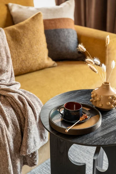 Stylish composition of modern living room. Stylish coffee table with tray, cup and yellow vase with dried flowers. Template.