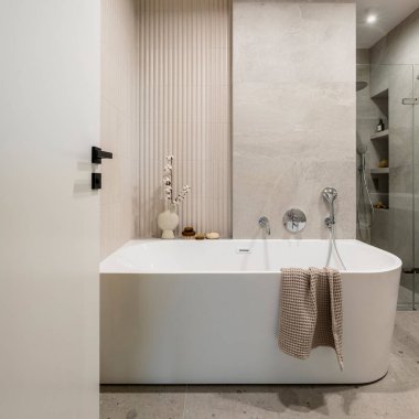 Lamella duvarlı, modern, parlak banyo. Gümüş musluğu ve kahverengi havlusu olan büyük beyaz bir banyo.. 