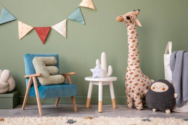 Yeşil duvarı, peluş oyuncakları, parlak halısı, mavi koltuğu, taburesi ve beyaz aksesuarları olan şık ve rahat çocuk odası iç tasarımının yaratıcı kompozisyonu. Gri ekoseli oyuncaklar için sepet. Şablon.