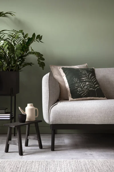 Stylish composition of living room interior. Modern sofa, design pillows, plants in metal pot and creative personal accessories. Eucalyptus green wall. Template. Copy space.