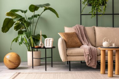 The stylish composition at living room interior with design beige sofa, coffee table, plants and elegant personal accessories. Brown pillow and plaid. Cozy apartment. Home decor.