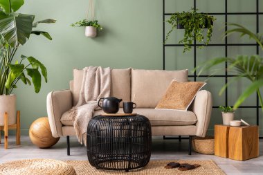 The stylish composition at living room interior with design beige sofa, black coffee table, plants and elegant personal accessories. Brown pillow and plaid. Cozy apartment. Home decor
