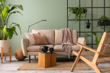 The stylish composition at living room interior with design beige sofa, wooden coffee table, plants and elegant personal accessories. Brown pillow and plaid. Cozy apartment. Home decor.