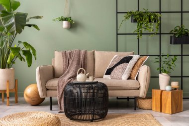 The stylish composition at living room interior with design beige sofa, black coffee table, plants and elegant personal accessories. Brown pillow and plaid. Cozy apartment. Home decor