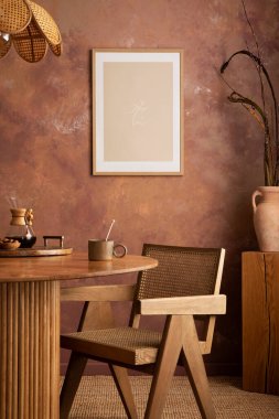Stylish boho vintage dining room interior with poster mock up. Round table with rattan chair, vase with dried flowers. Brown wall and rattan lamp. Mock up poster. Template. 
