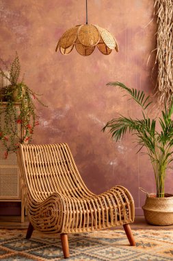 Stylish boho vintage dining room interior with rattan armachair, carpet, commode and plants. Brown wall and rattan lamp. Home decor. Template. 