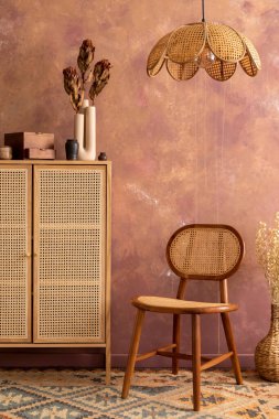 Stylish boho vintage dining room interior with rattan commode, chair, vase with drierd flowers and personal accessories. Brown wall and rattan lamp. Template. 
