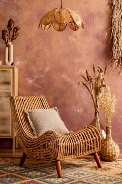 Stylish boho vintage dining room interior with rattan armachair, pillow carpet, commode and plants. Brown wall and rattan lamp. Home decor. Template. 